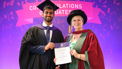 Two people in graduation attire; one hands a certificate to the other